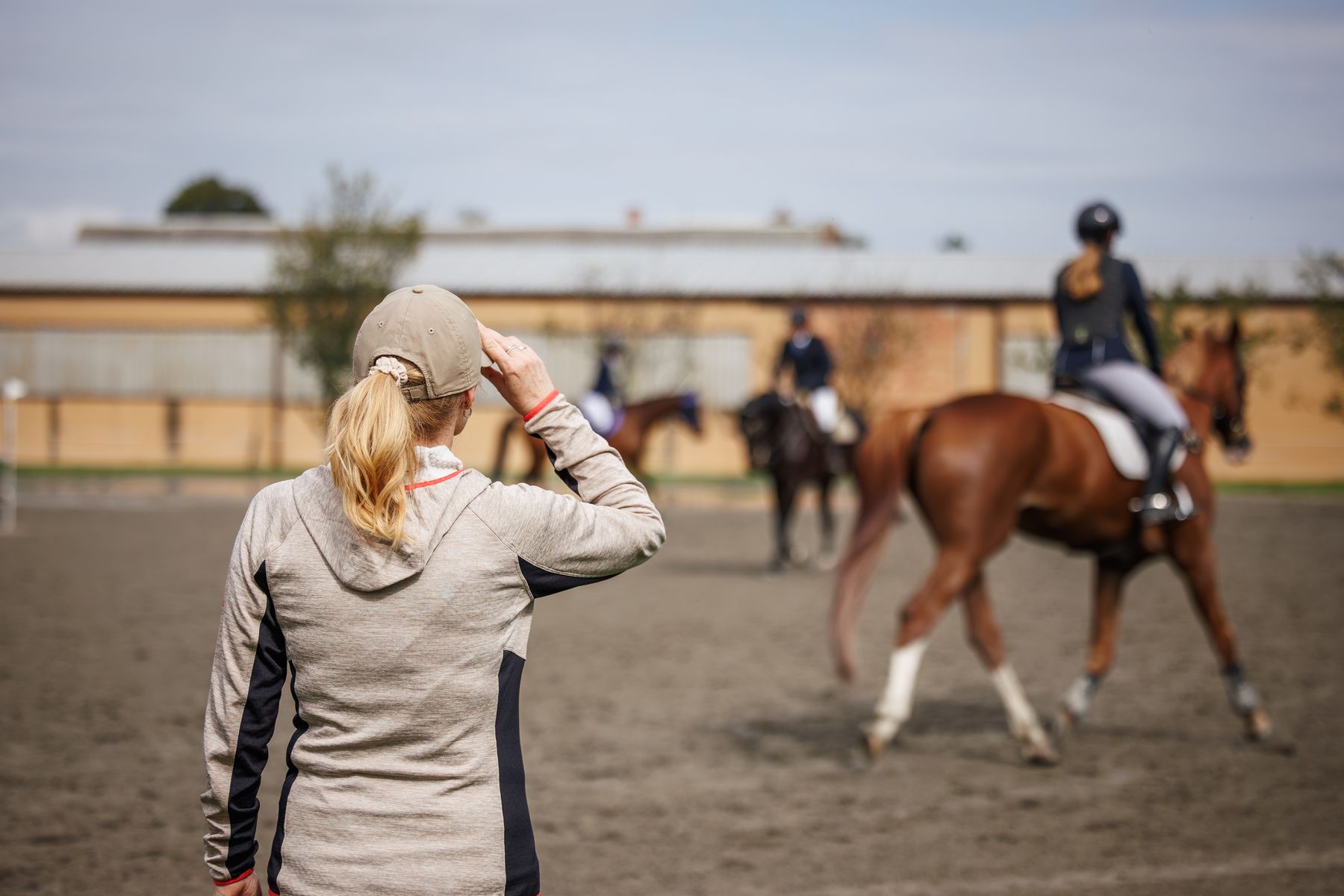 A riding instructor watching her riders during a lesson in an outdoor arena